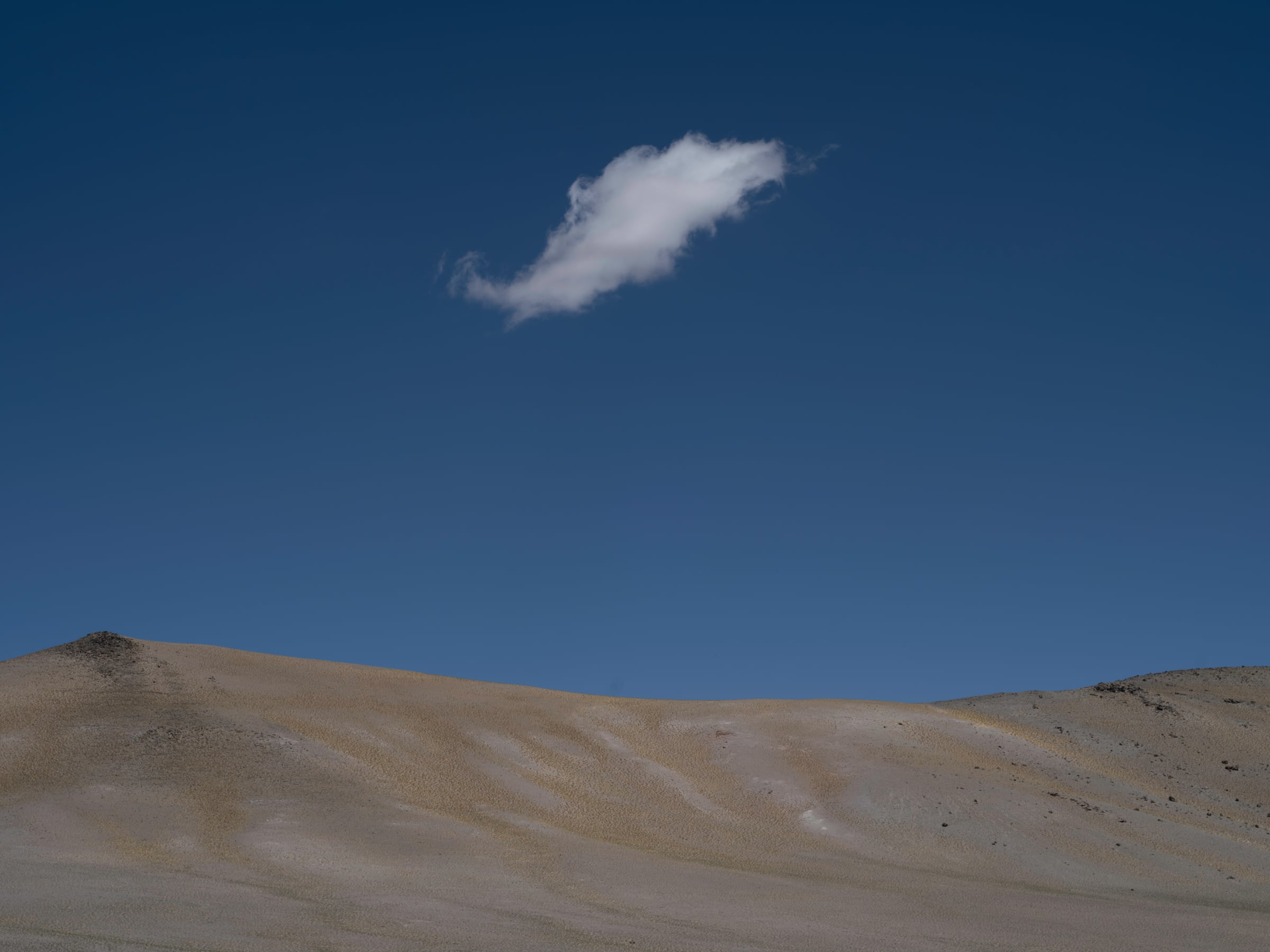 A single white cloud above bare hills in a deep blue sky